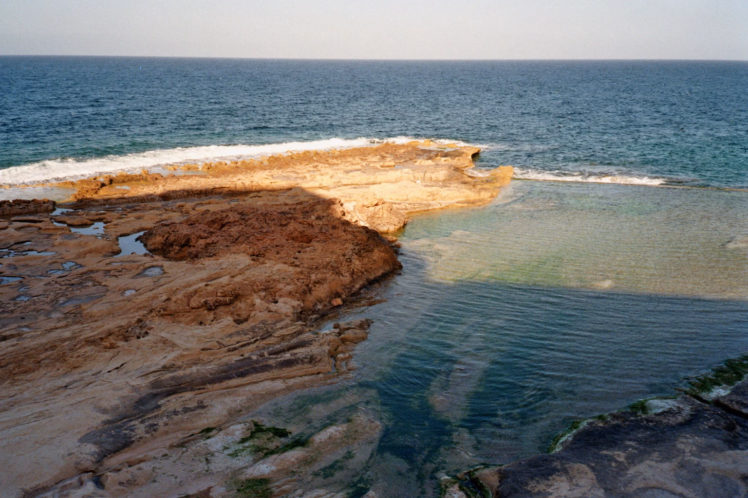 Ein natürlicher Felspool an der felsigen Küste von Malta bei Sonnenschein.